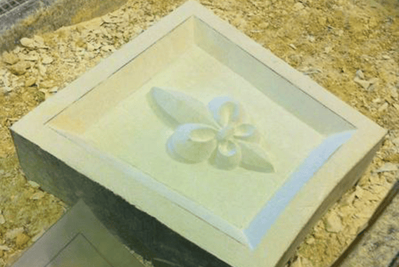 8640beca5fd175f6d3aa18ac.45373955 Sculpture en pierre représentant une fleur taillée dans un bloc, élément décoratif architectural en cours de réalisation