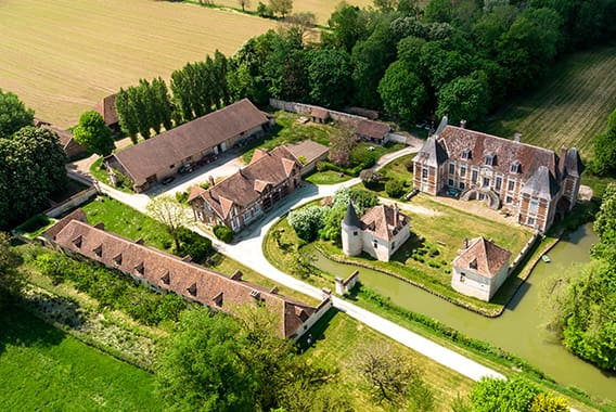 Château de Villemereuil 8 - © Studio OG Vue aérienne d’un château entouré de douves, jardins et dépendances, au cœur d’un paysage verdoyant de campagne dans l’Aube en Champagne